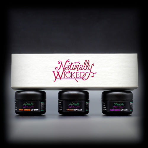 Naturally Wicked Lip Balm Trio Box On Top Of 3 Luxury Fruit Filled White Lip Balm Containers; Coconut, Dark Fruits & Sweet Orange