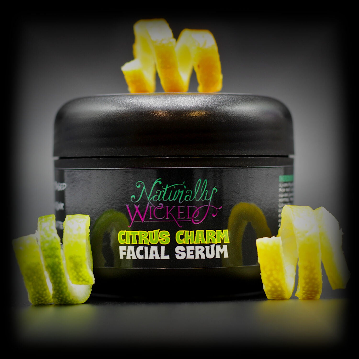Naturally Wicked Citrus Charm Serum in sleek black packaging, garnished with spirals of lemon and lime.