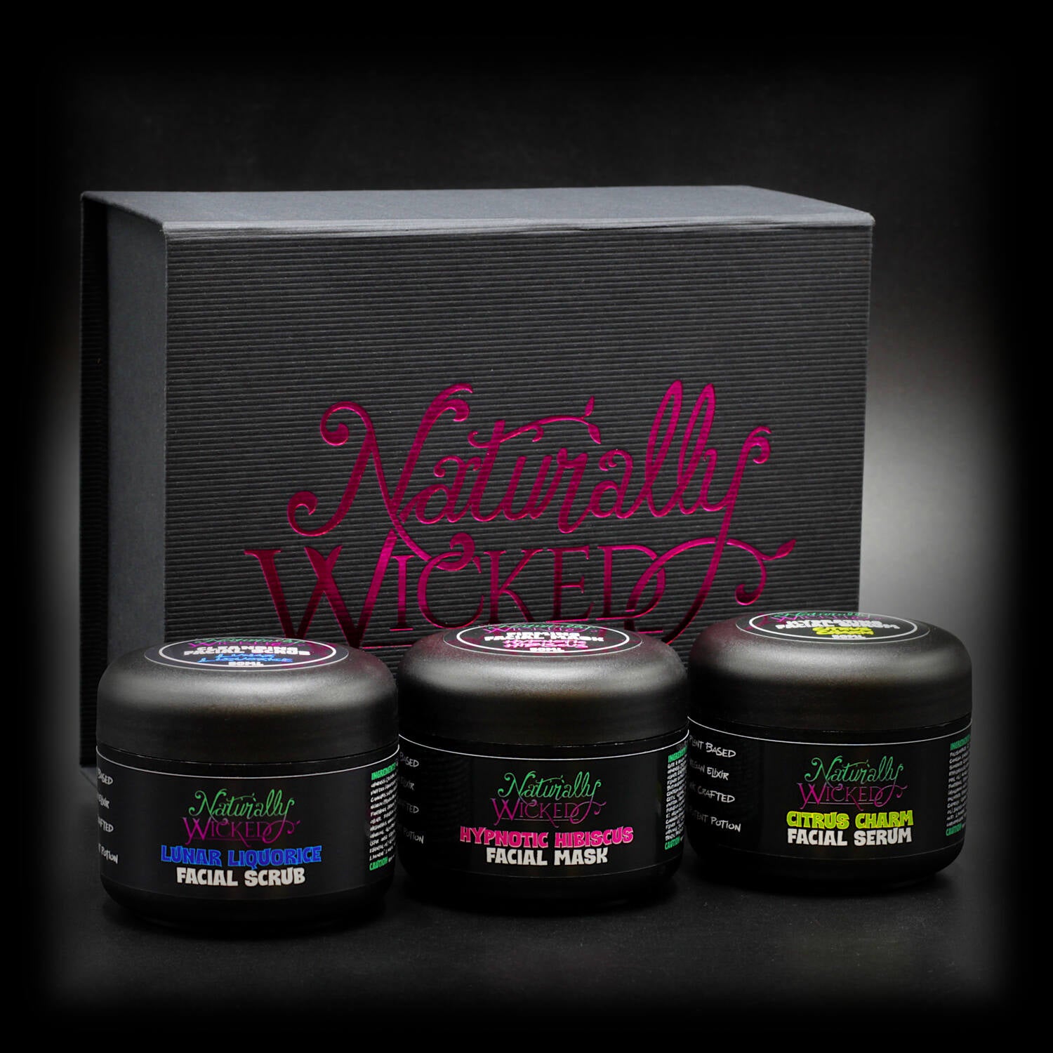 Naturally Wicked skincare trio with Lunar Liquorice Facial Scrub, Hypnotic Hibiscus Facial Mask, and Citrus Charm Facial Serum in front of a stylish black gift box.