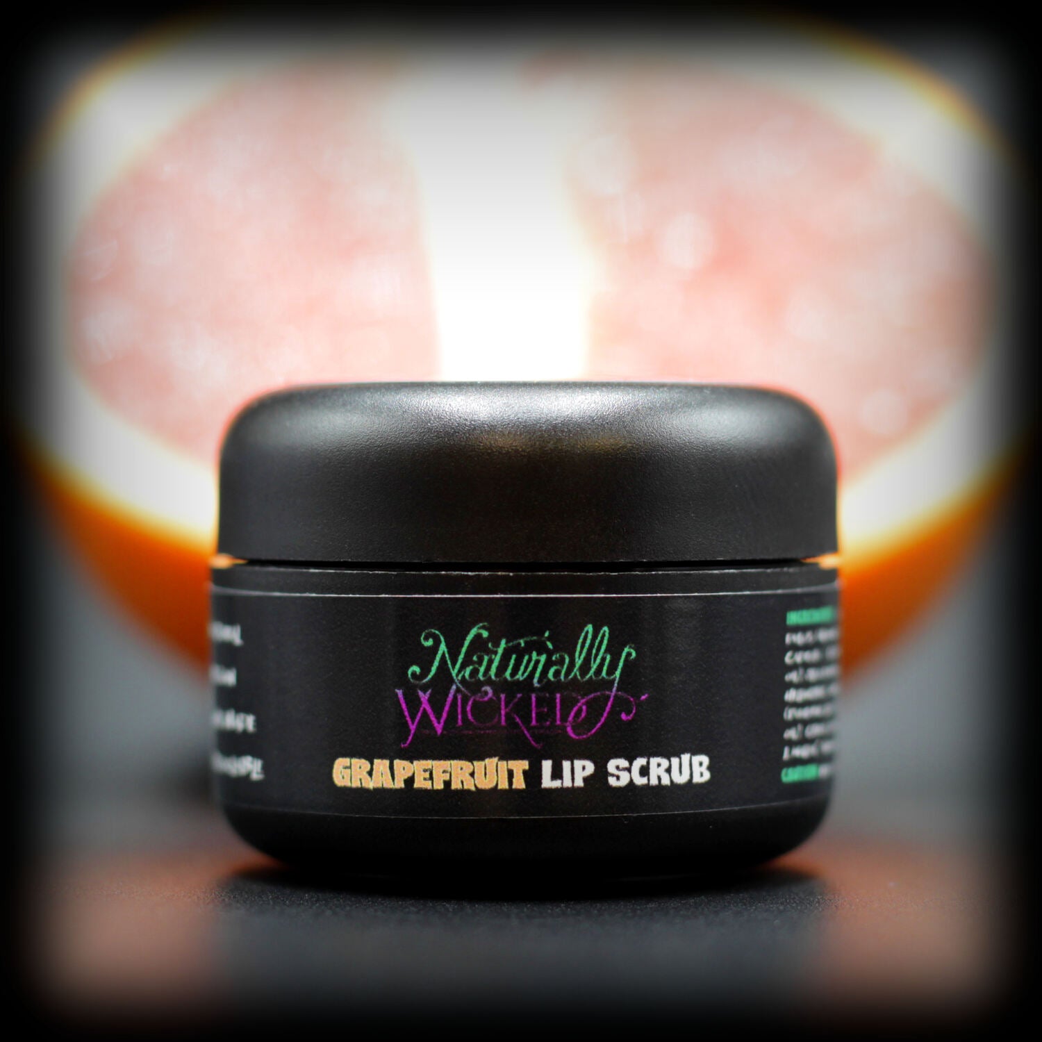 Naturally Wicked Grapefruit Lip Scrub In Luxury Black Container Beside a Fresh Sliced Grapefruit