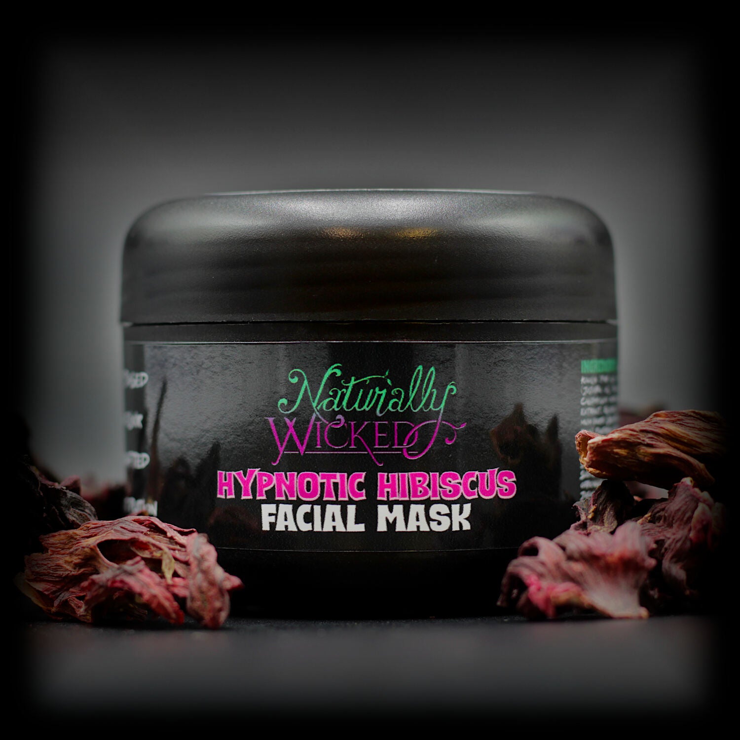 Naturally Wicked Hypnotic Hibiscus Facial Mask in black tub, accented by dried hibiscus petals.
