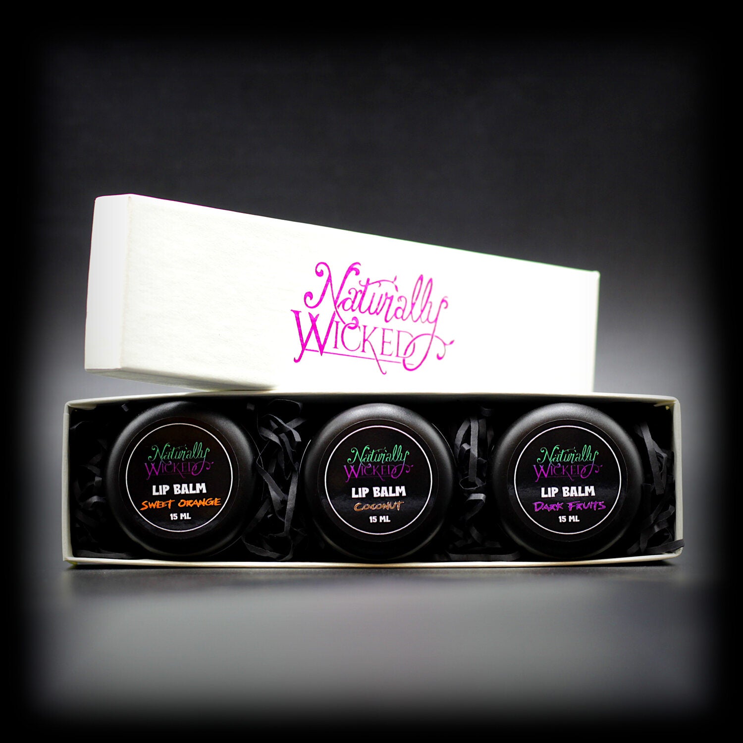 Naturally Wicked Lip Balm Trio Inner Box Revealed With Lids Of Orange, Dark Fruit & Coconut Lip Balm Peaking Out Amongst Luxury Gift Packaging