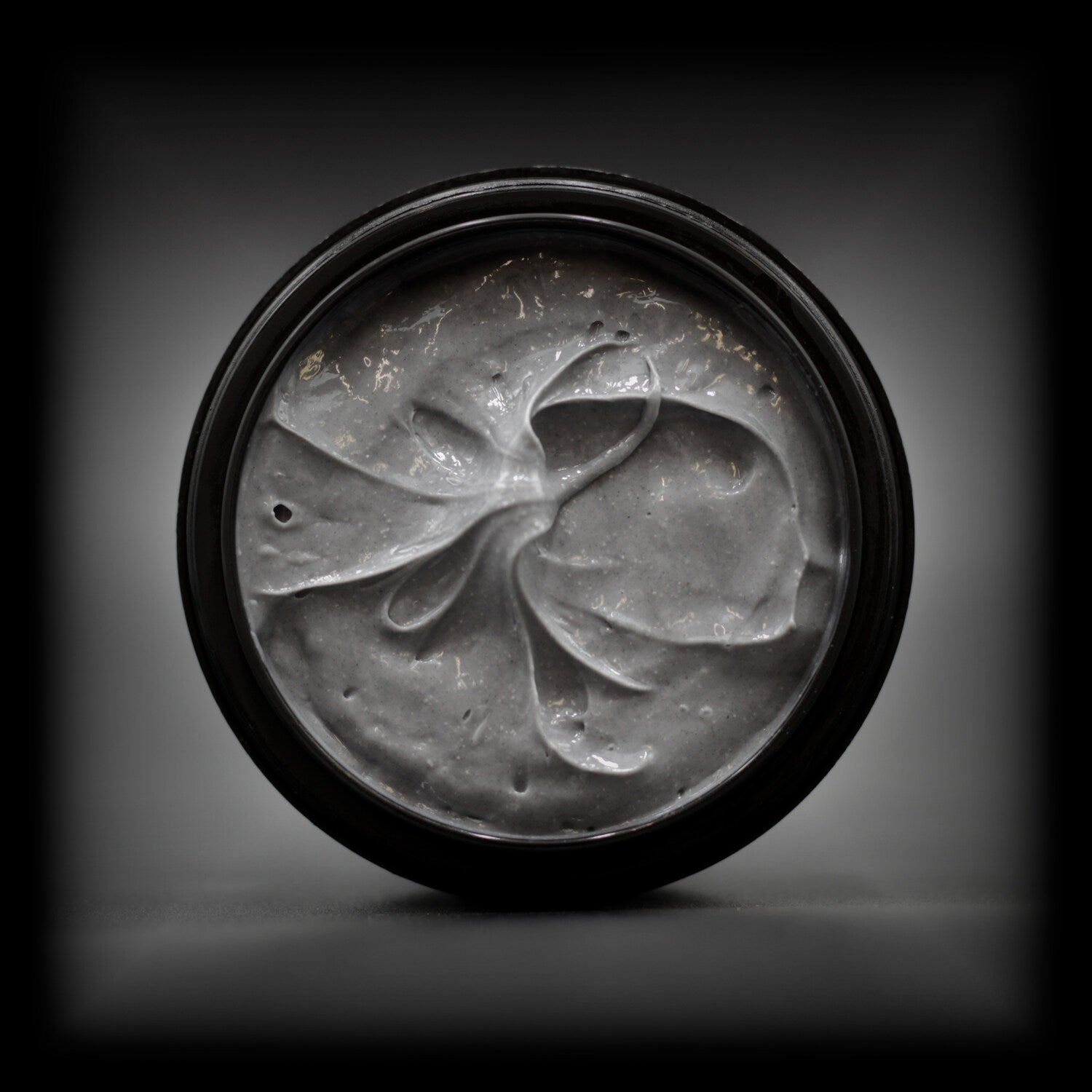 Top view of Naturally Wicked Lunar Liquorice Facial Scrub with smooth, dark grey texture in an open tub.