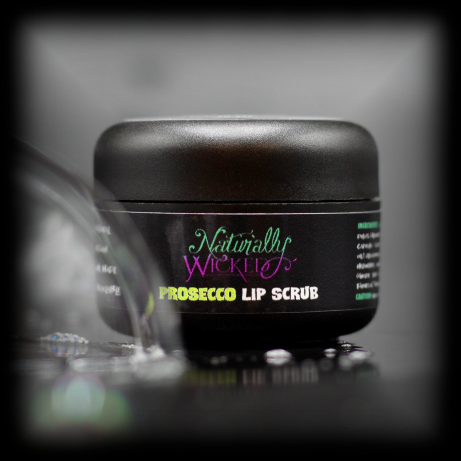 Naturally Wicked Prosecco Lip Scrub In Luxury Black Container Beside a Clear Shiny Bubble