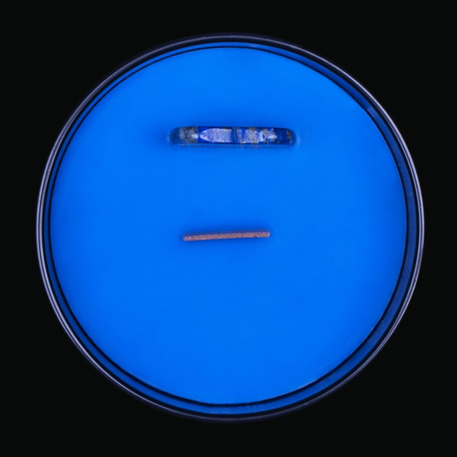 Naturally Wicked Spellbinding Ouija Crystal Candle View From Above Shows Blue Smooth Plant-based Wax, Featuring A Wooden Wick And A Carved Sodalite  Spell Crystal Planchette. All Situated Within A Black Gloss Glass Container. A Spine-tingling Gift