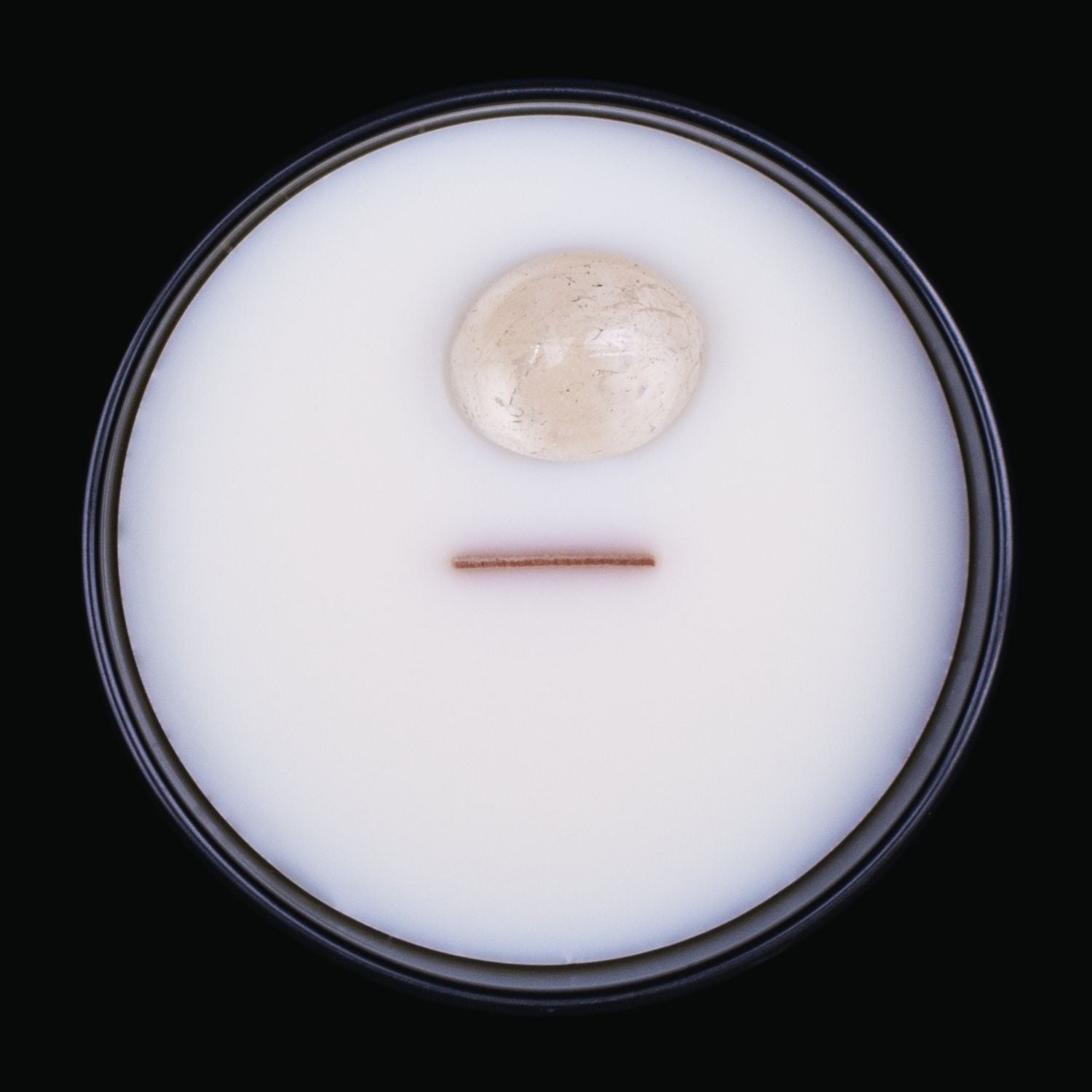 Naturally Wicked Spellbinding Peace Crystal Candle View From Above Shows Pure White Smooth Plant-based Wax, Featuring A Wooden Wick And Clear Quartz Spell Crystal. All Situated Within A Black Gloss Glass Container. Give The Gift Of Peace